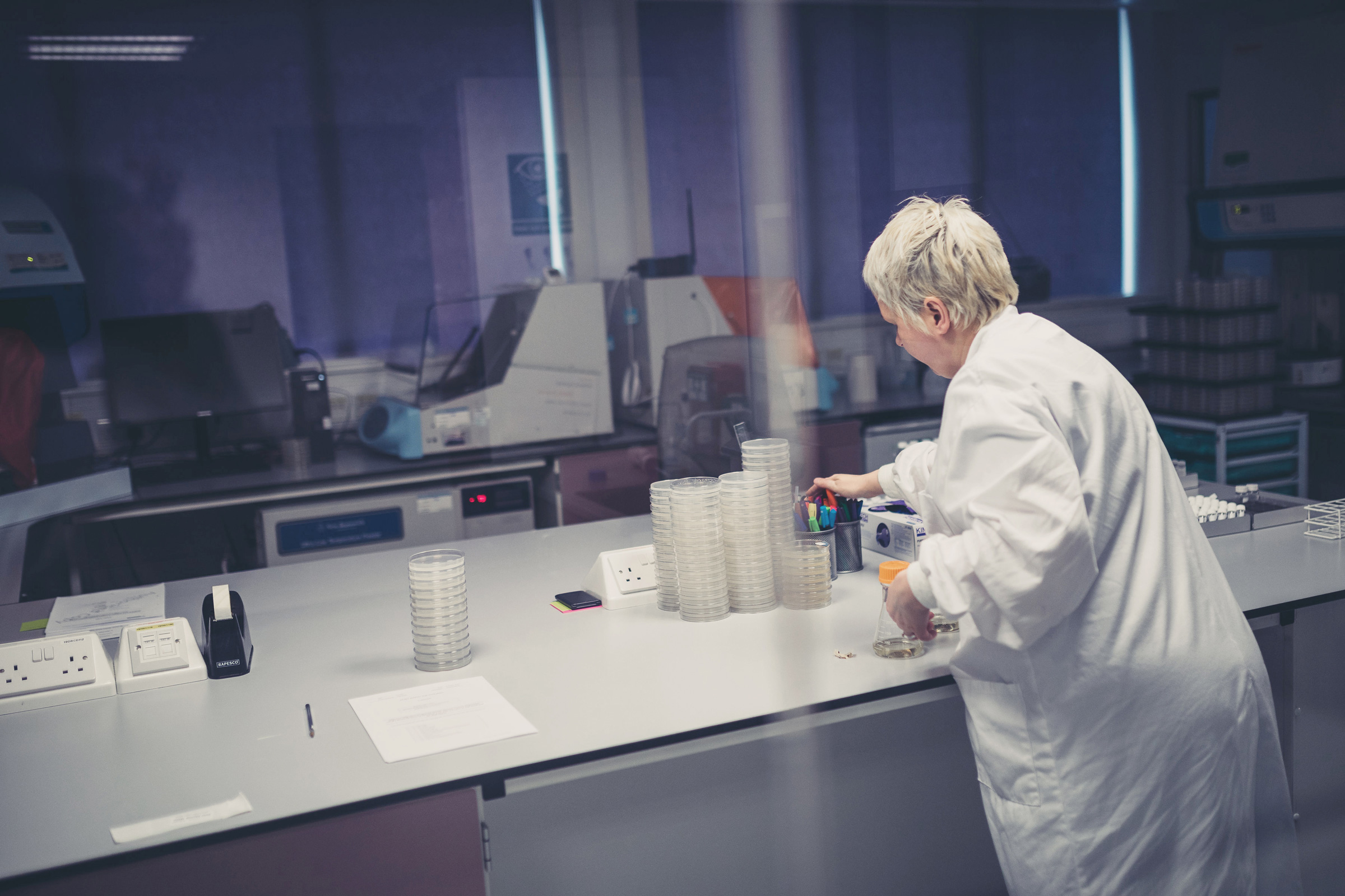 Laboratory professional in a white coat handling and organizing test tubes on a bench in a modern laboratory environment.